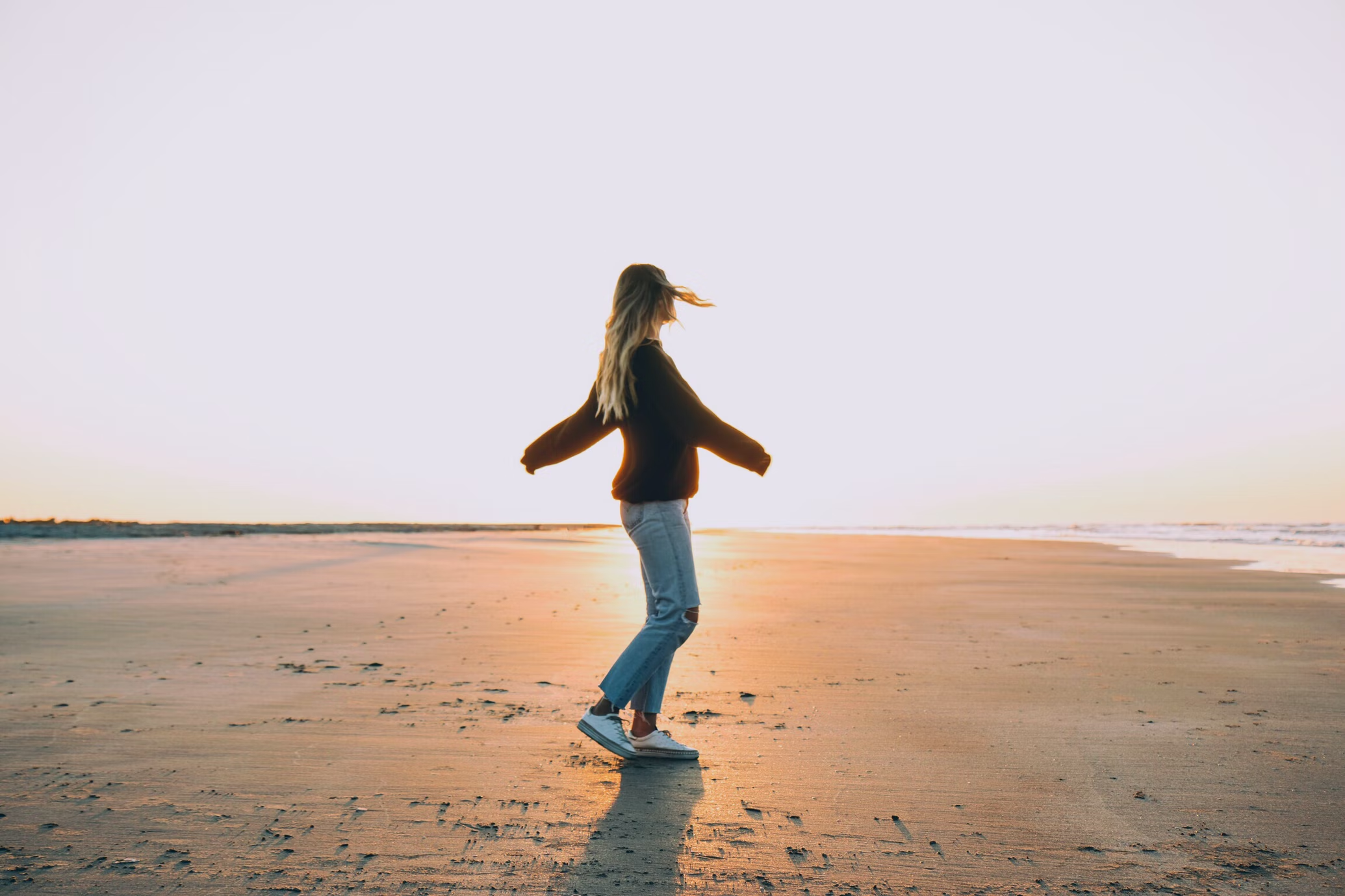 a young adult female walking on a beach with Fall attire on